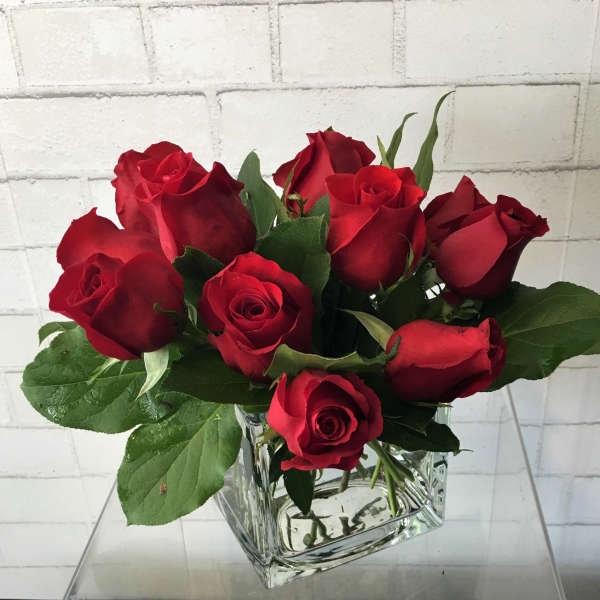 Red roses arranged in a clear square glass vase