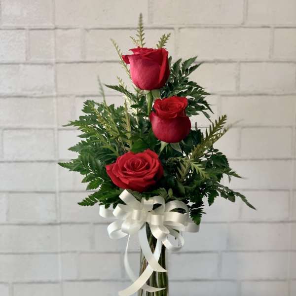 Three red roses in a clear glass vase with a white ribbon