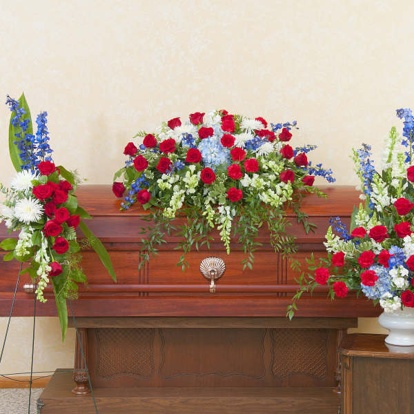 Casket spray with red, white, and blue flowers on a wooden casket