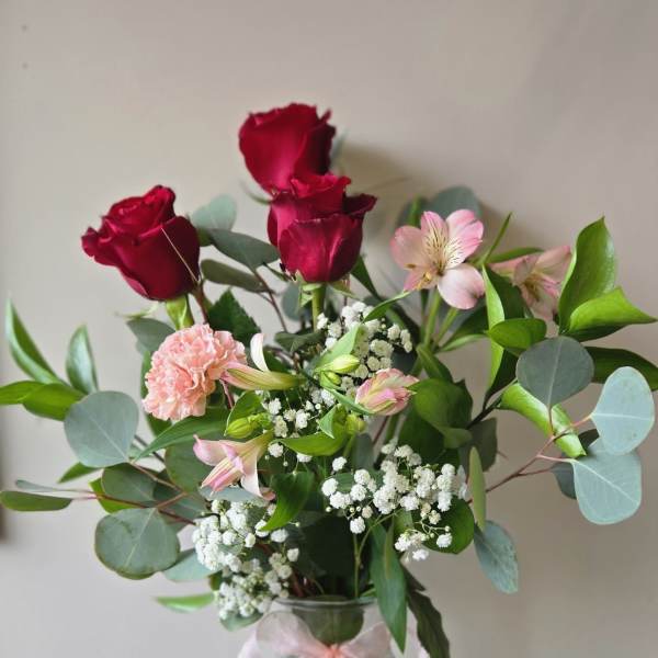 Bouquet of red roses and pink flowers in a glass vase with a ribbon