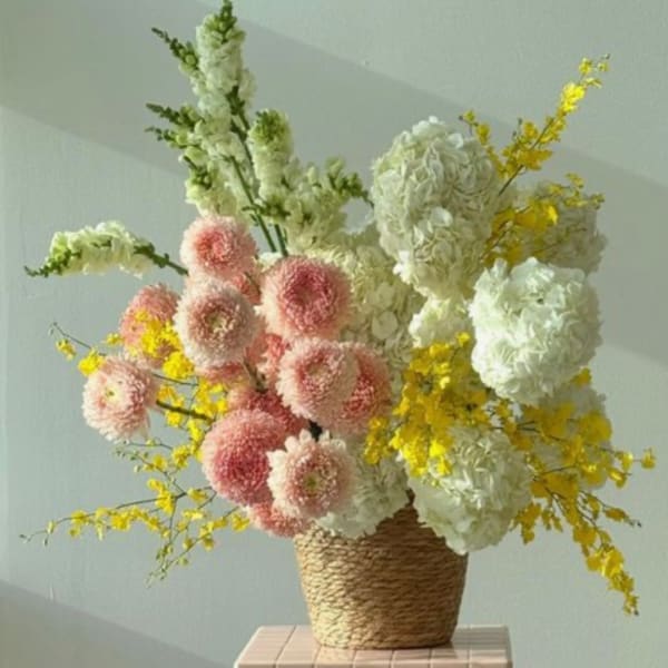 Tall floral arrangement in a woven basket with pink, white, and yellow blooms