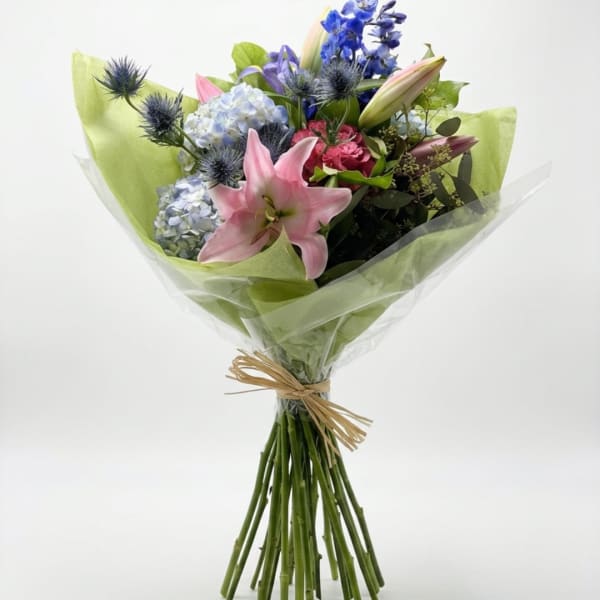 Bouquet of pink lilies, blue hydrangeas, and purple flowers wrapped in green paper