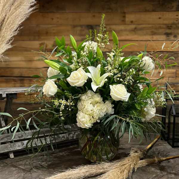 White roses and lilies arranged in a glass vase with greenery