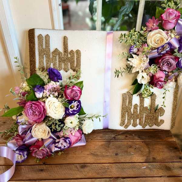 Religious book-style floral tribute with pink, white, and purple blooms on a Holy Bible plaque