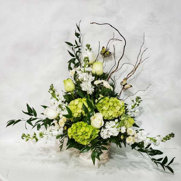 Tall floral arrangement with white roses, green hydrangeas, and butterflies in a low container