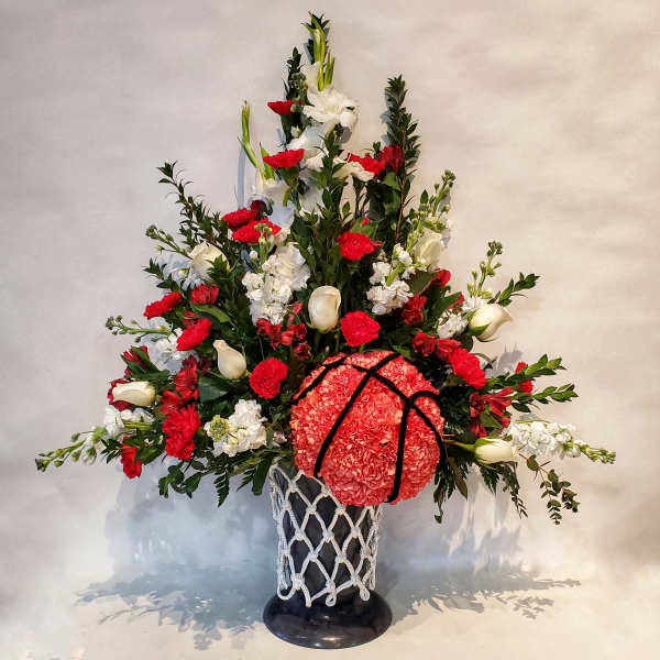 Tall red and white floral arrangement in a black vase with rope netting