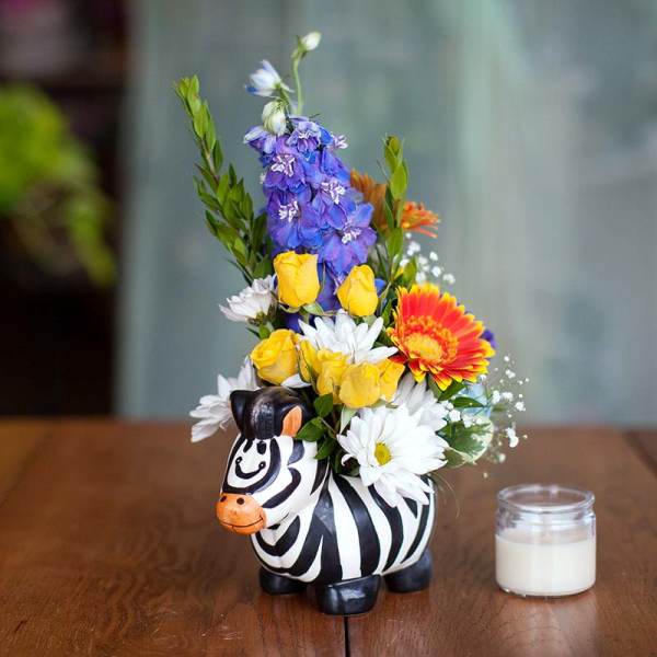 Colorful flower arrangement in a zebra-shaped container beside a small candle.
