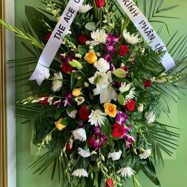 Large funeral wreath with mixed flowers and white condolence ribbons