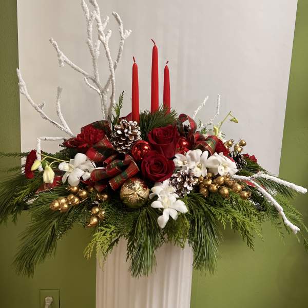 Holiday centerpiece with red roses, white flowers, and red candles in a white pedestal vase