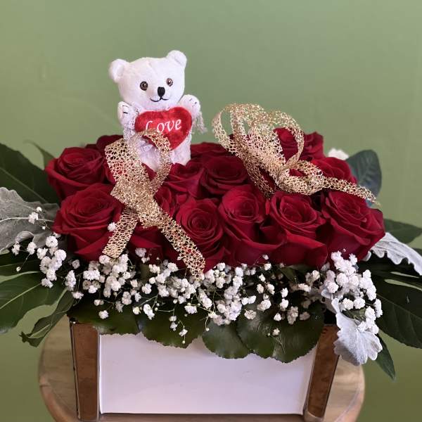 Red roses arranged in a white box with a small teddy bear and ribbon