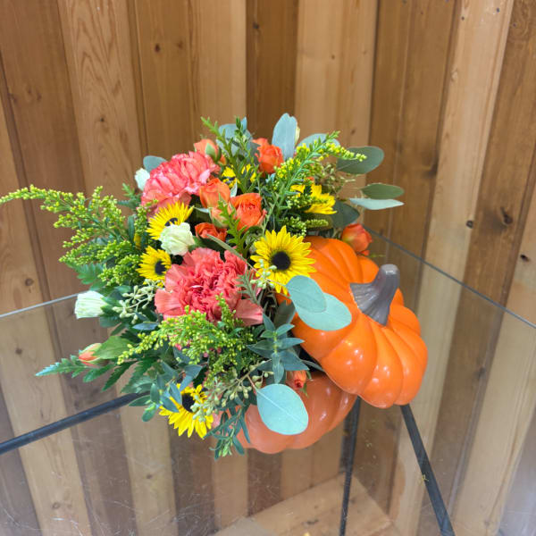 Fall bouquet with sunflowers, orange roses, and pink carnations beside a pumpkin
