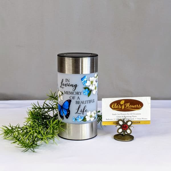 Memorial candle with floral butterfly design and a small greenery sprig