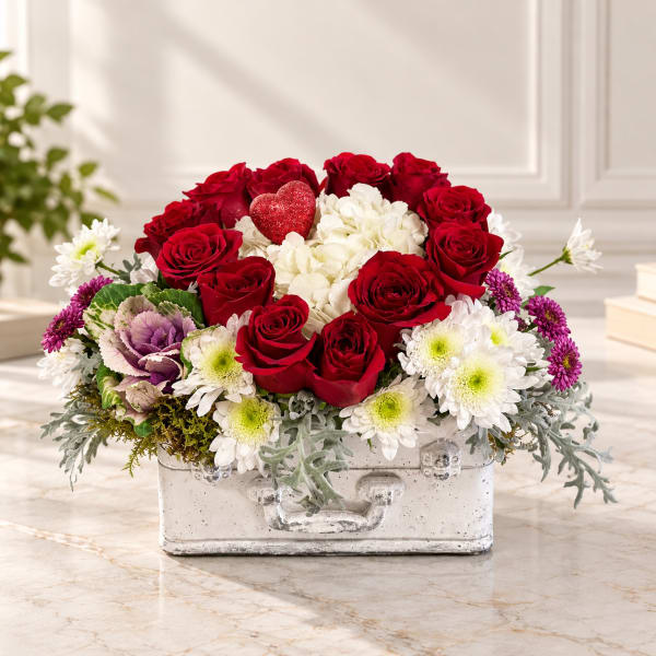Red roses and white flowers arranged in a white metal container with a heart accent