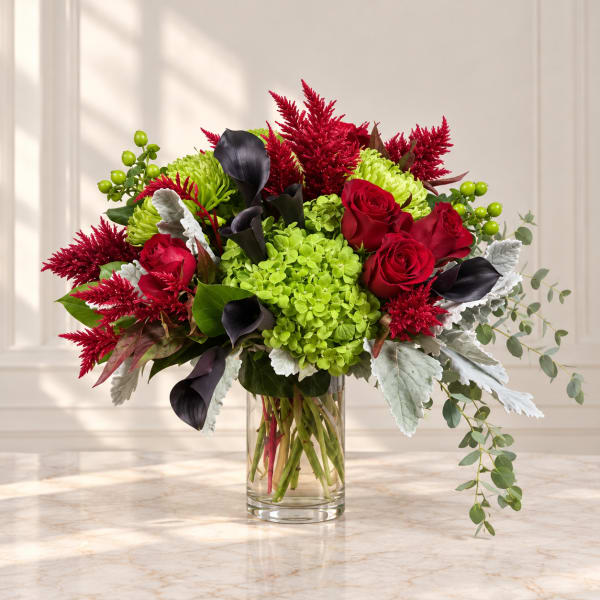 Bouquet of red roses, green hydrangea, and dark calla lilies in a glass vase.