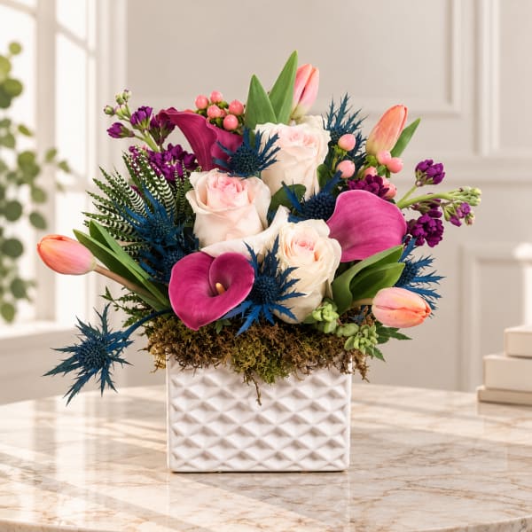 Mixed bouquet of roses, tulips, and calla lilies in a white vase