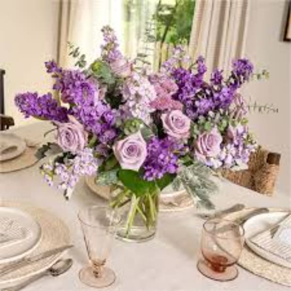 Purple and lavender floral centerpiece in a clear glass vase on a set table