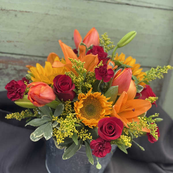 Bouquet of orange lilies, red roses, and a sunflower in a metal bucket