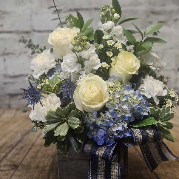 Cream roses and blue hydrangeas in a wooden box with a ribbon.