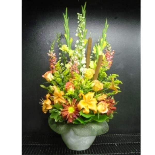 Tall autumn-toned arrangement with orange lilies, roses, and cattails in a frosted vase