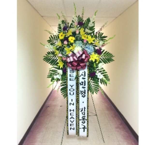 Tall standing funeral spray with yellow lilies, mixed blooms, and message ribbons on an easel