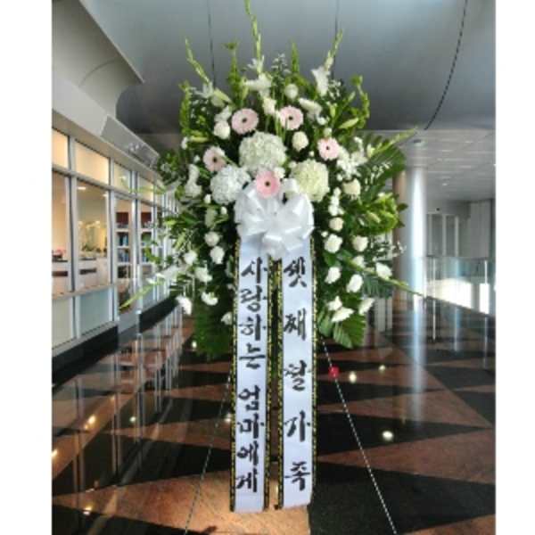Large standing sympathy spray with white and pale pink flowers and long message ribbons on an easel.