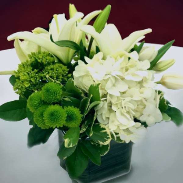White lilies and hydrangeas with green pompons in a dark vase