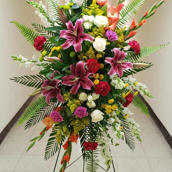Tall standing spray of pink lilies, red carnations, white roses and mixed flowers on a metal easel