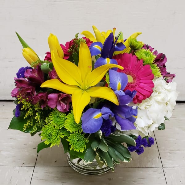 Bright mixed bouquet with yellow lilies, purple irises, pink gerberas, and white hydrangeas in a glass vase