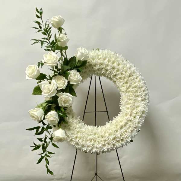 White floral wreath with roses on a black stand
