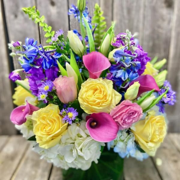 Colorful bouquet with yellow roses, pink calla lilies, and blue-purple flowers in a vase