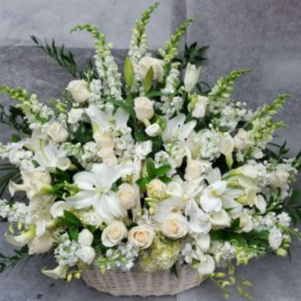 White floral arrangement in a woven basket with lilies and roses