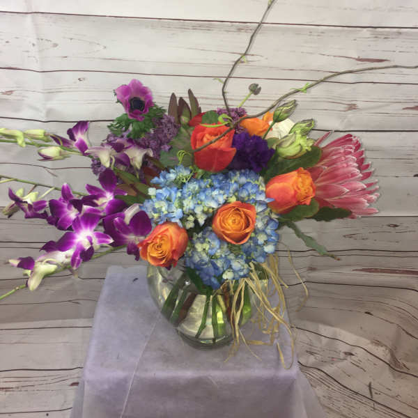 Colorful mixed bouquet in a glass vase with orange roses and blue hydrangea