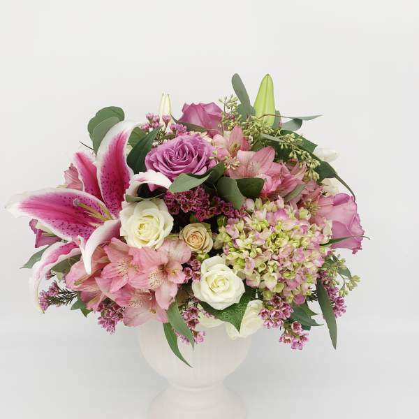 Pink and white mixed flower arrangement with lilies and roses in a white urn-style vase