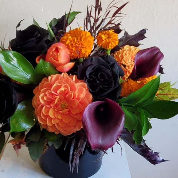 Orange and dark floral arrangement in a black vase with calla lilies and roses