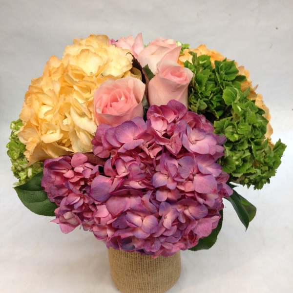 Bouquet of pink roses and hydrangeas in a burlap-wrapped container