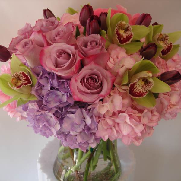 Pink and lavender bouquet with roses, hydrangeas, and orchids in a glass vase
