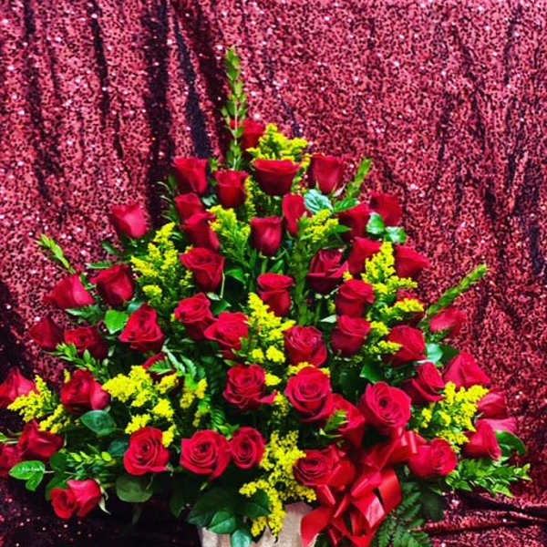 Large bouquet of red roses with yellow filler flowers in a white basket
