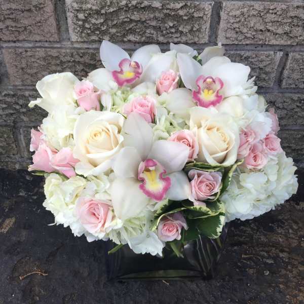 White and pink bouquet with roses, orchids, and hydrangeas in a black vase