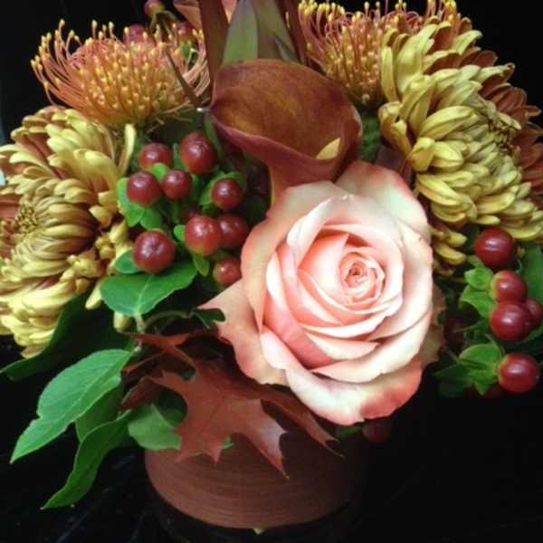 Compact autumn-toned arrangement with a peach rose, bronze blooms, and berries in a brown vase