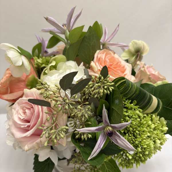 Short arrangement of peach and pink roses with white and green blooms in a clear glass vase