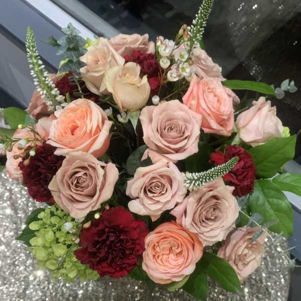 Bouquet of blush and peach roses with burgundy carnations