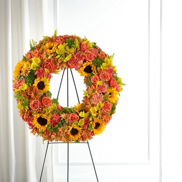 Circular floral wreath on a black stand with sunflowers and roses