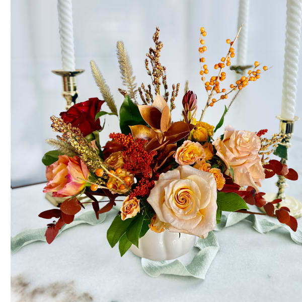 Autumn floral centerpiece with roses in a white vase and lit candles