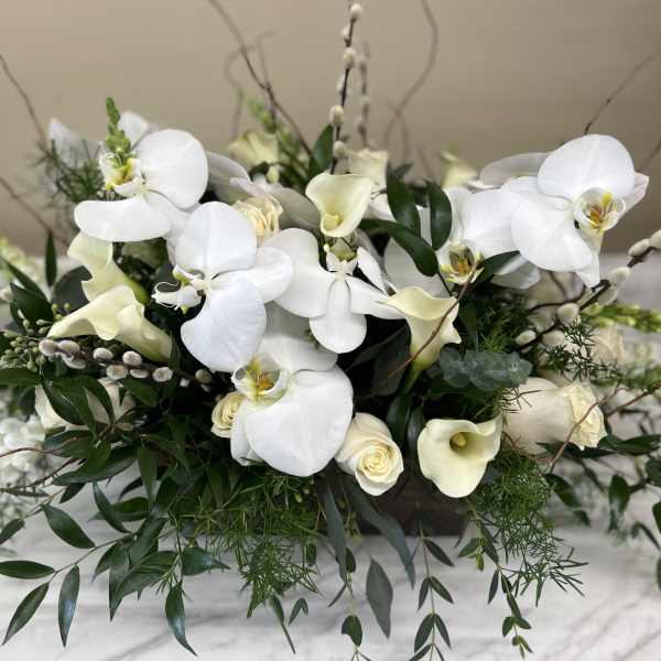 White orchids and calla lilies arranged with greenery in a low container