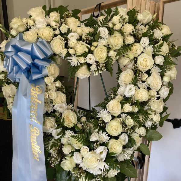 Large white floral funeral wreath with a blue ribbon on an easel