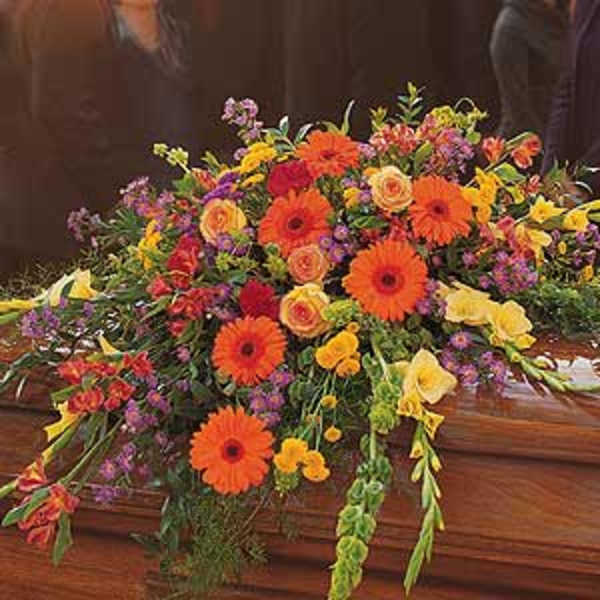 Bright mixed casket spray with orange gerberas and yellow roses on a wooden casket