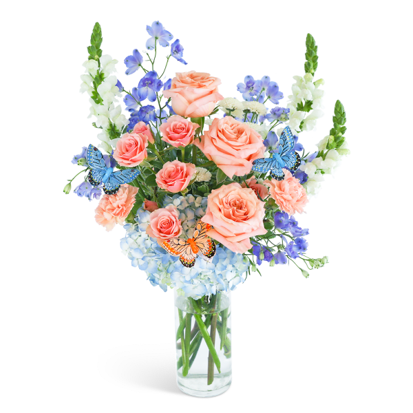 Peach roses and blue flowers in a clear glass vase with butterfly picks
