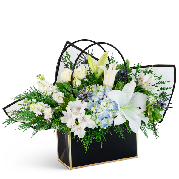 White lilies, roses, and blue hydrangea in a black gift bag