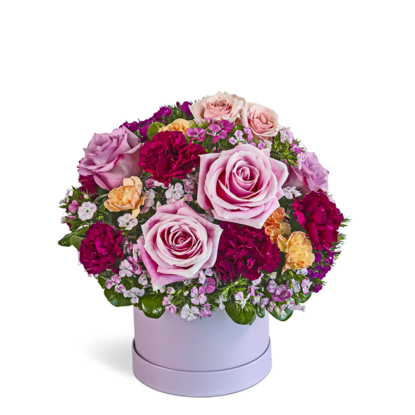 Round arrangement of pink roses, red carnations and small blooms in a light pink hatbox container