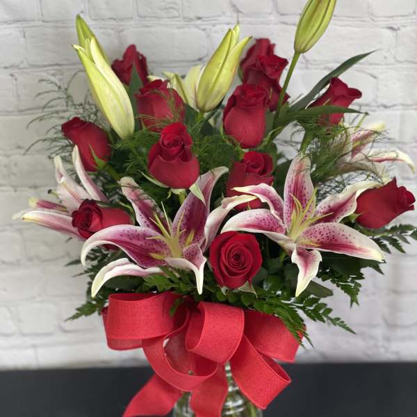 Bouquet of red roses and pink lilies in a glass vase with a red ribbon